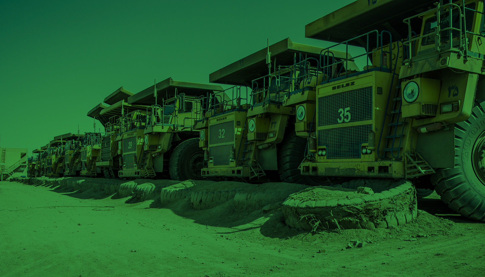 A fleet of heavy mining dump trucks parked in a row at a staging area, showcasing the scale of equipment used in Okuni Africa's industrial projects.